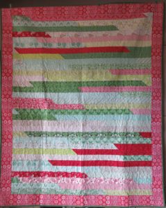 Photo of Jelly Roll Race quilt with border made of red, green and white christmas-themed fabrics.