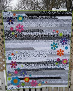 Black and White Jelly Roll Race quilt with colored appliqued flowers