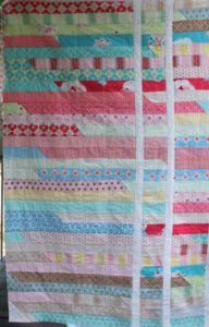 Photo of Jelly Roll Race quilt that has been cut and resewn with two white strips sewn in vertically
