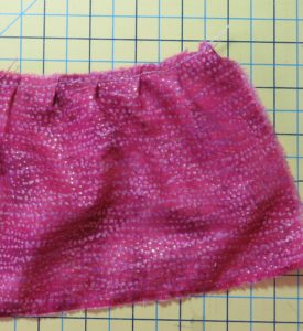 Photograph of pink fabric pleated with ruffler sewing machine feet for gathering fabrics. Ruffler set to one pleat every 12 stitches.