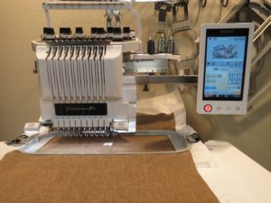 Photo of Brother PR1000e embroidery machine with hoop loaded with brown linen and design set on screen