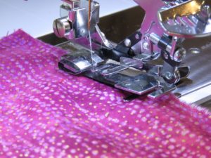 Photo of pink fabric placed under ruffler, one of two sewing machine feet for gathering fabric
