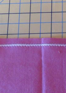 Photo showing pink fabric with white dental floss encased in zig zag stitch to create a gather