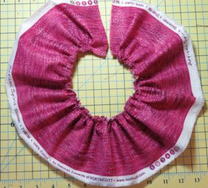 Photograph of pink fabric pleated with ruffler sewing machine feet for gathering fabrics. Ruffler set to one pleat per stitch.