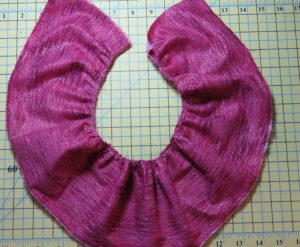 Photograph of pink fabric pleated with ruffler sewing machine feet for gathering fabrics. Ruffler set to one pleat per 6 stitches.