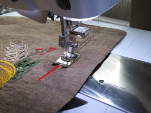 Photo of cutwork tea towel being hemstitched. Red arrow indicated center line