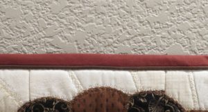 Photo of red and brown flange binding wrapped around to front of quilt wall hanging.
