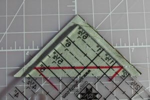 Photo of triangle ruler with line drawn at seam line for trimming down over-sized half square triangles