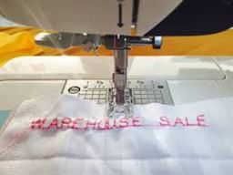 photo of Warehouse Sale embroidered on a piece of white fabric.