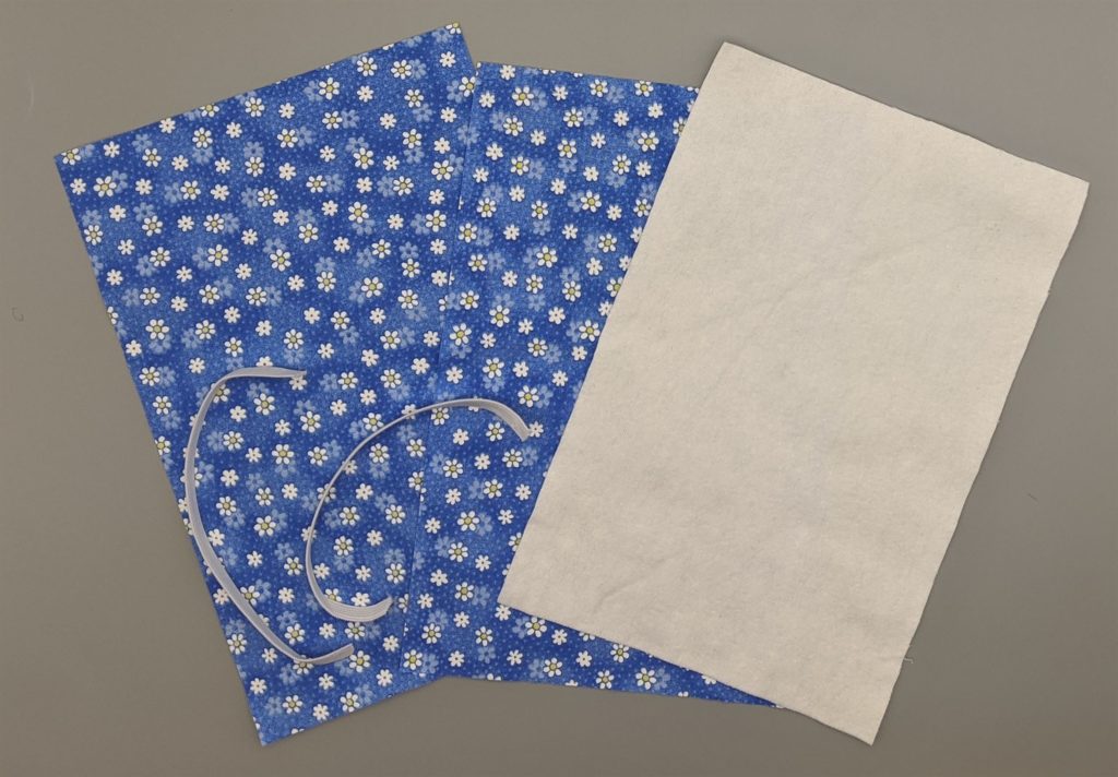 photograph of two pieces of blue flowered fabric, one piece of white flannel and two 7" pieces of 1/4" elastic to make cotton face masks.